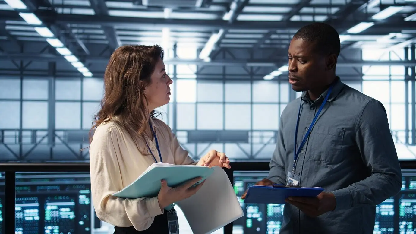 Радостные администраторы встречаются в дата-центре для просмотра отчётов и пожимают друг другу руки.